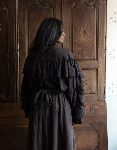 Person wearing a dark layered dress standing in front of a wooden door.