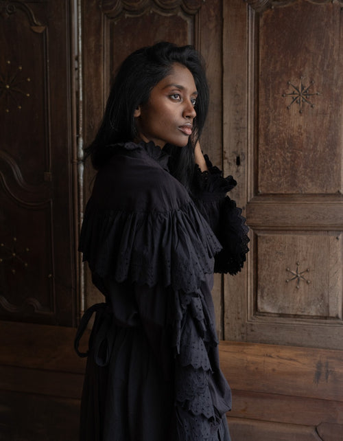 Woman in a black dress standing against a wooden paneled wall.