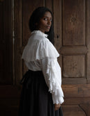 Woman wearing a white blouse with ruffled sleeves against a wooden panel background