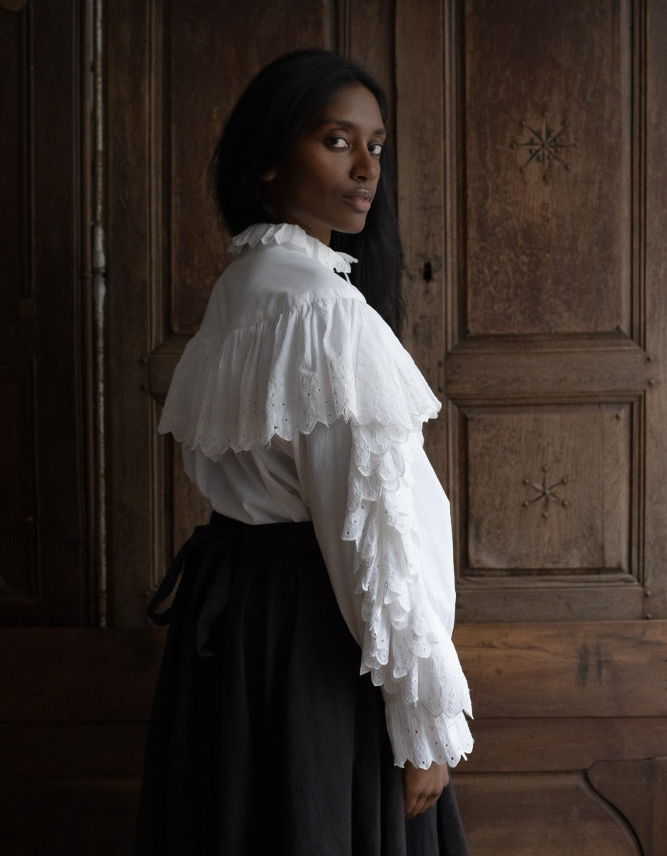 Woman wearing a white blouse with ruffled sleeves against a wooden panel background