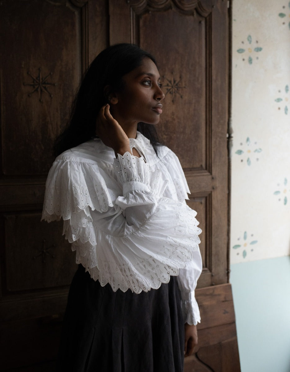 Woman wearing a white lace blouse standing in a room with wooden paneling.