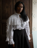 Woman wearing a white blouse with ruffled sleeves and black skirt in a room with wooden paneling.