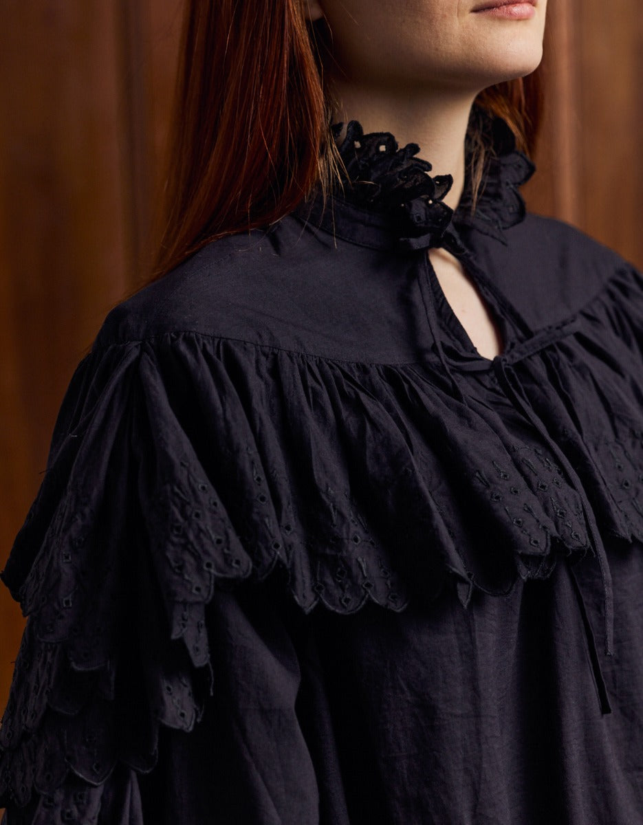 Close-up of a person wearing a black ruffled blouse against a brown background