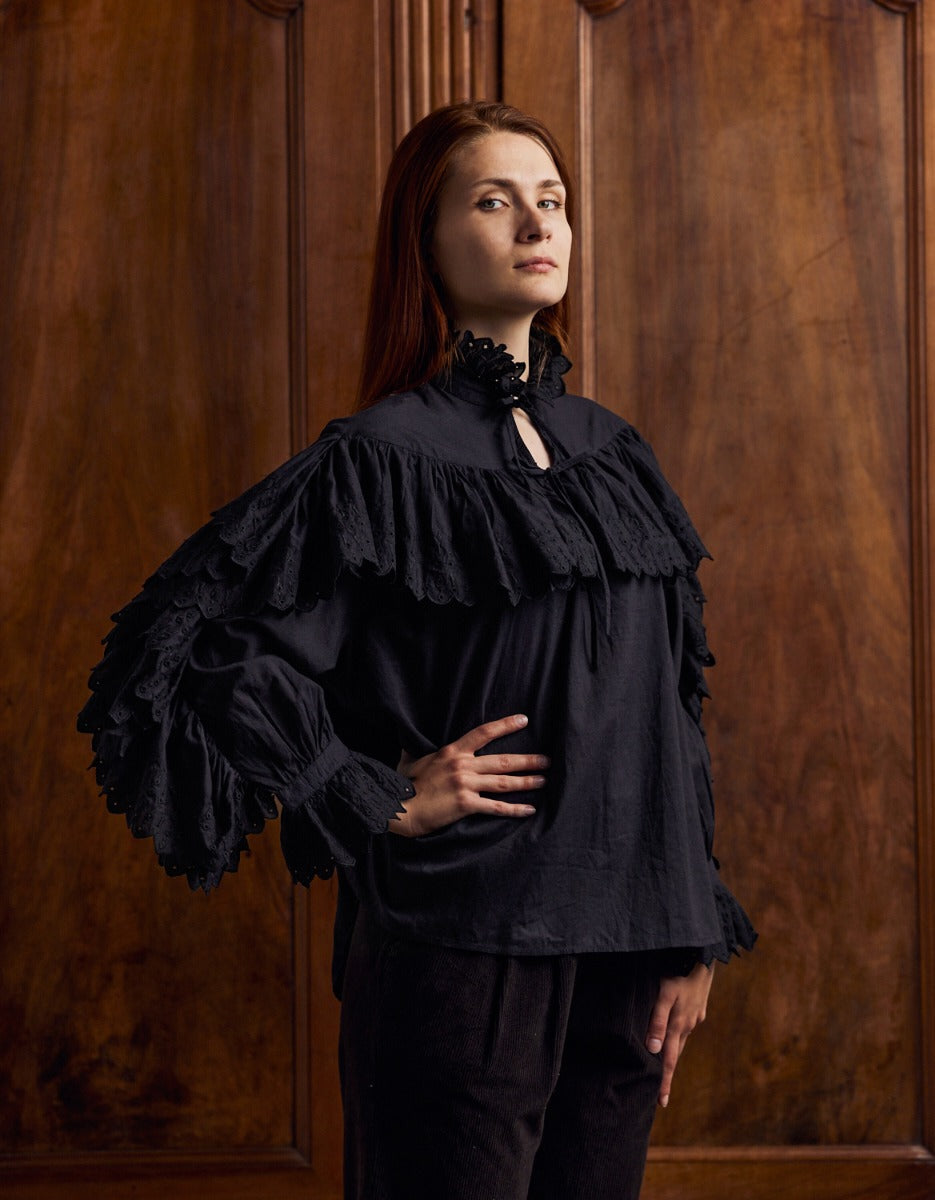 Woman wearing a black ruffled blouse against a wooden paneled wall