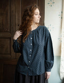 Woman wearing a dark blue polka dot blouse in a room with wooden paneling.