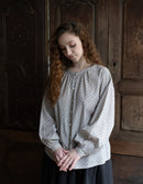 Woman wearing a polka dot blouse in a dimly lit room with wooden walls.