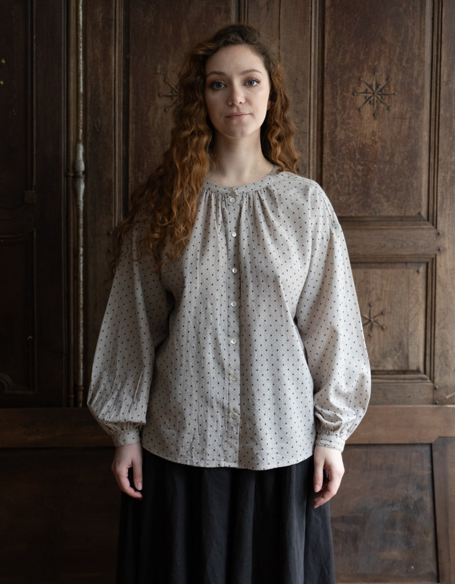 Woman wearing a patterned blouse standing in front of a wooden door.