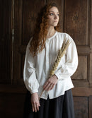 Woman in a white blouse holding dried plants against a wooden background