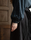 Person wearing a dark blue long-sleeve top with white patterns and a black skirt in a rustic setting.