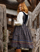 Woman in a traditional outfit standing in front of wooden walls.