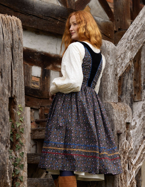 Woman in a traditional outfit standing in front of wooden walls.