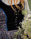 Close-up of a person wearing a black velvet dress with floral details, surrounded by flowers.
