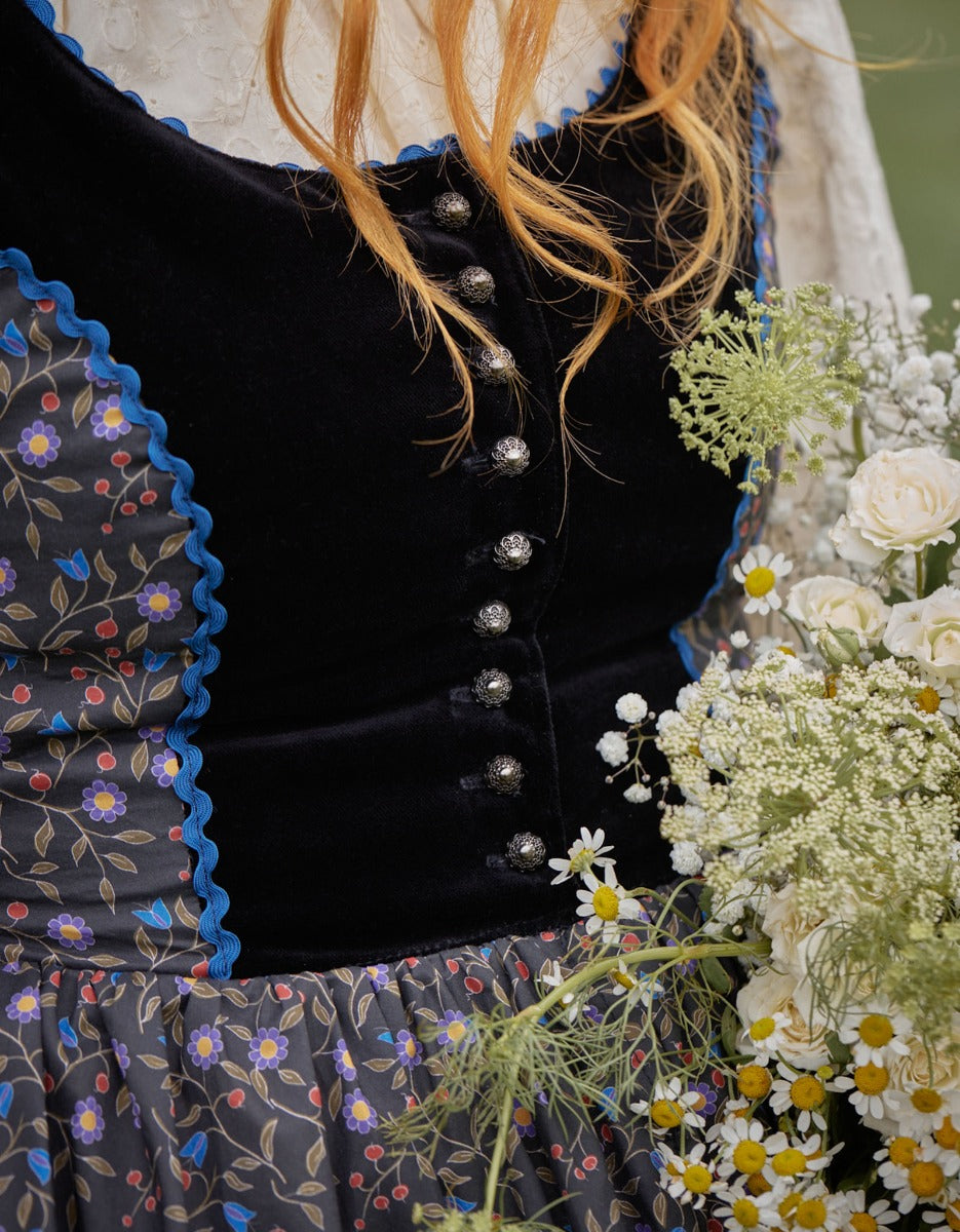 Close-up of a person wearing a black velvet dress with floral details, surrounded by flowers.