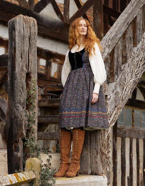 Woman in historical attire standing in front of a wooden building
