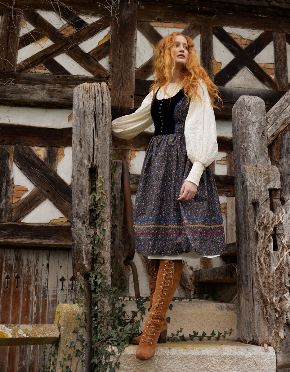 Woman in historical attire standing in front of a wooden half-timbered building.