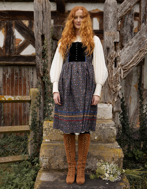 Woman in traditional outfit standing in front of rustic wooden architecture