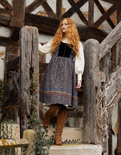 Woman in historical attire standing on stone steps in a rustic setting