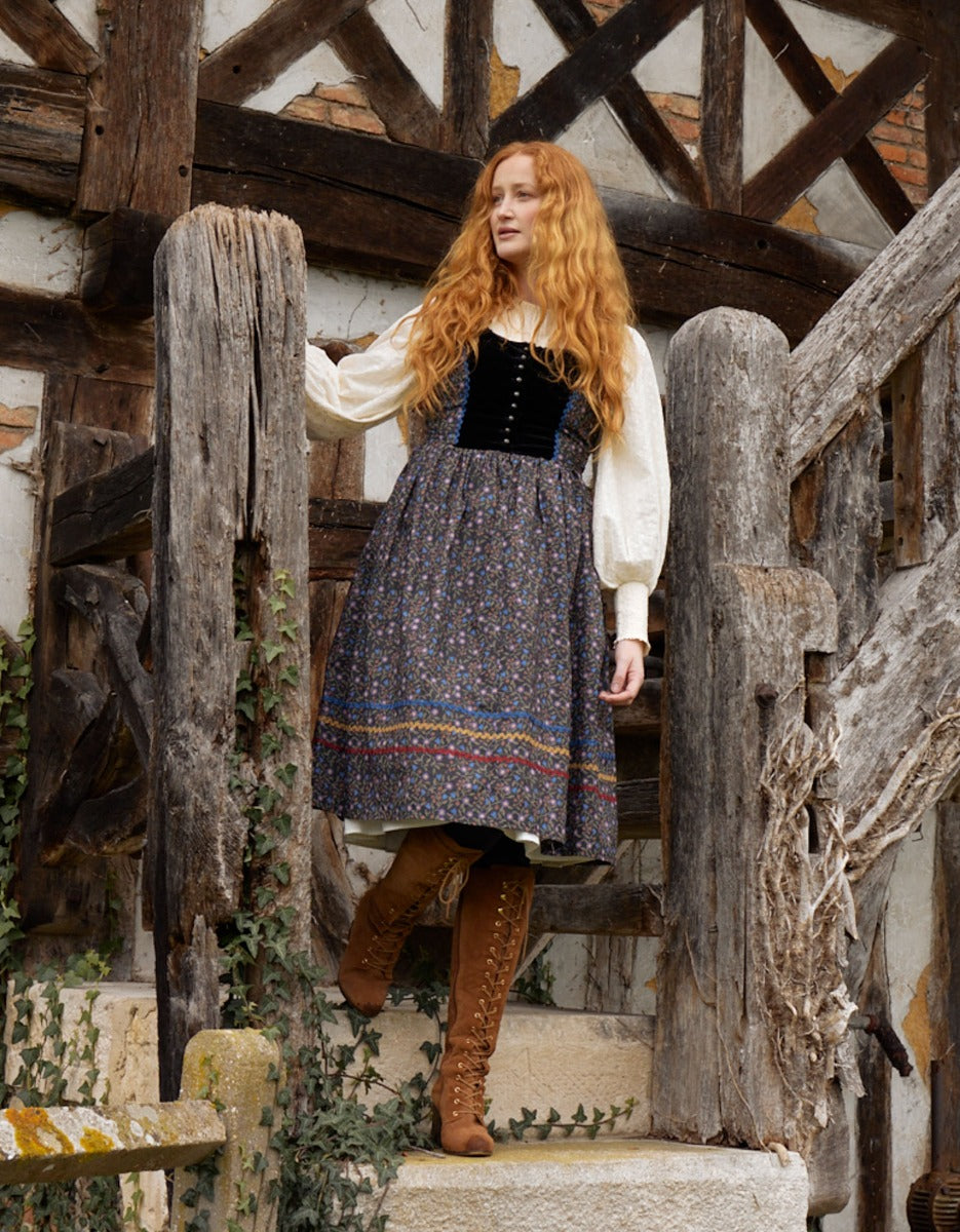 Woman in historical attire standing on stone steps in a rustic setting