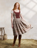 Woman in a traditional dress standing on hay with a white wall background