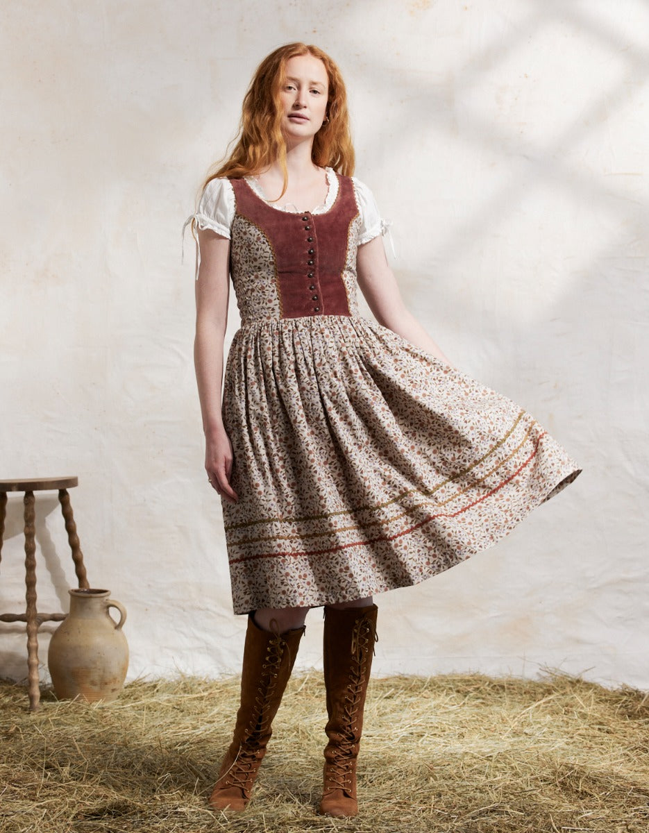 Woman in a traditional dress standing on hay with a white wall background
