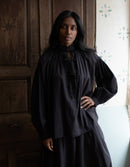 Woman wearing a black dress standing in a room with wooden paneling.