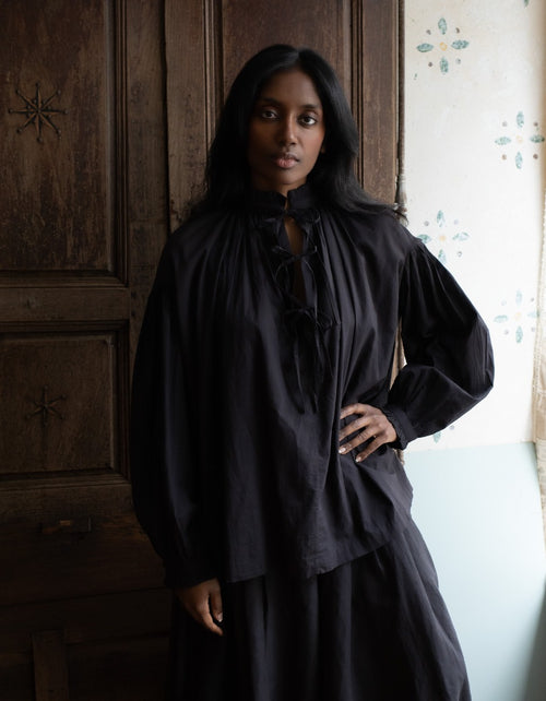 Woman wearing a black dress standing in a room with wooden paneling.