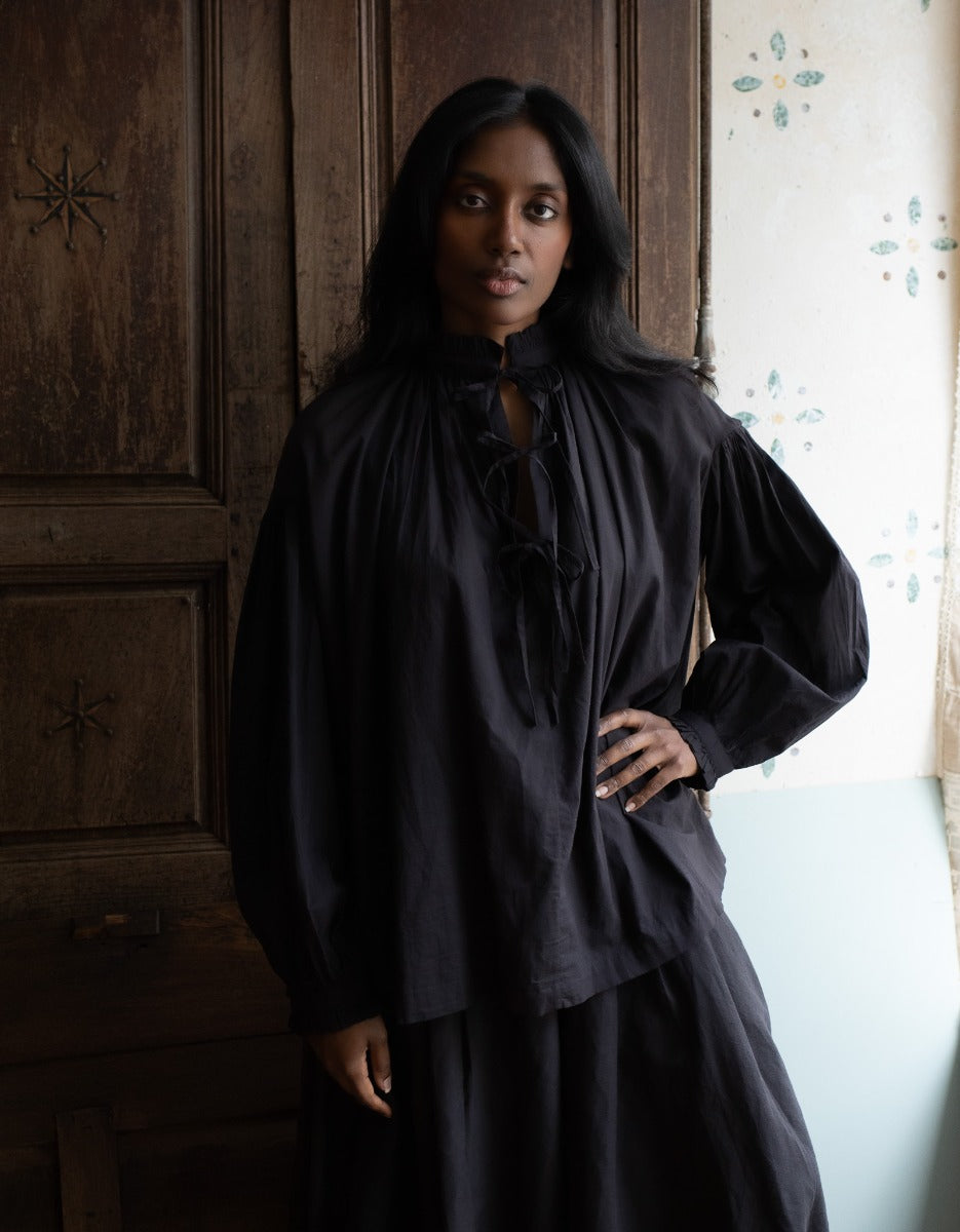 Woman wearing a black dress standing in a room with wooden paneling.
