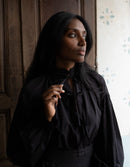 Woman wearing a black blouse with a high collar in a dimly lit room.