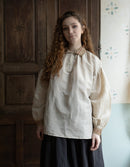 Woman wearing a historical-style blouse with intricate details in a room with wooden paneling.