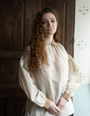 Woman wearing a historical-style blouse with intricate details in a room with wooden paneling.