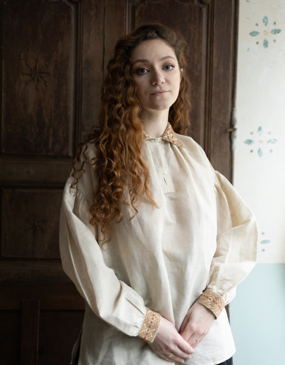 Woman wearing a historical-style blouse with intricate details in a room with wooden paneling.