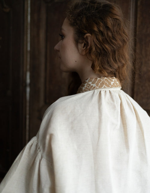 Person wearing a white dress with a high collar in a dimly lit room