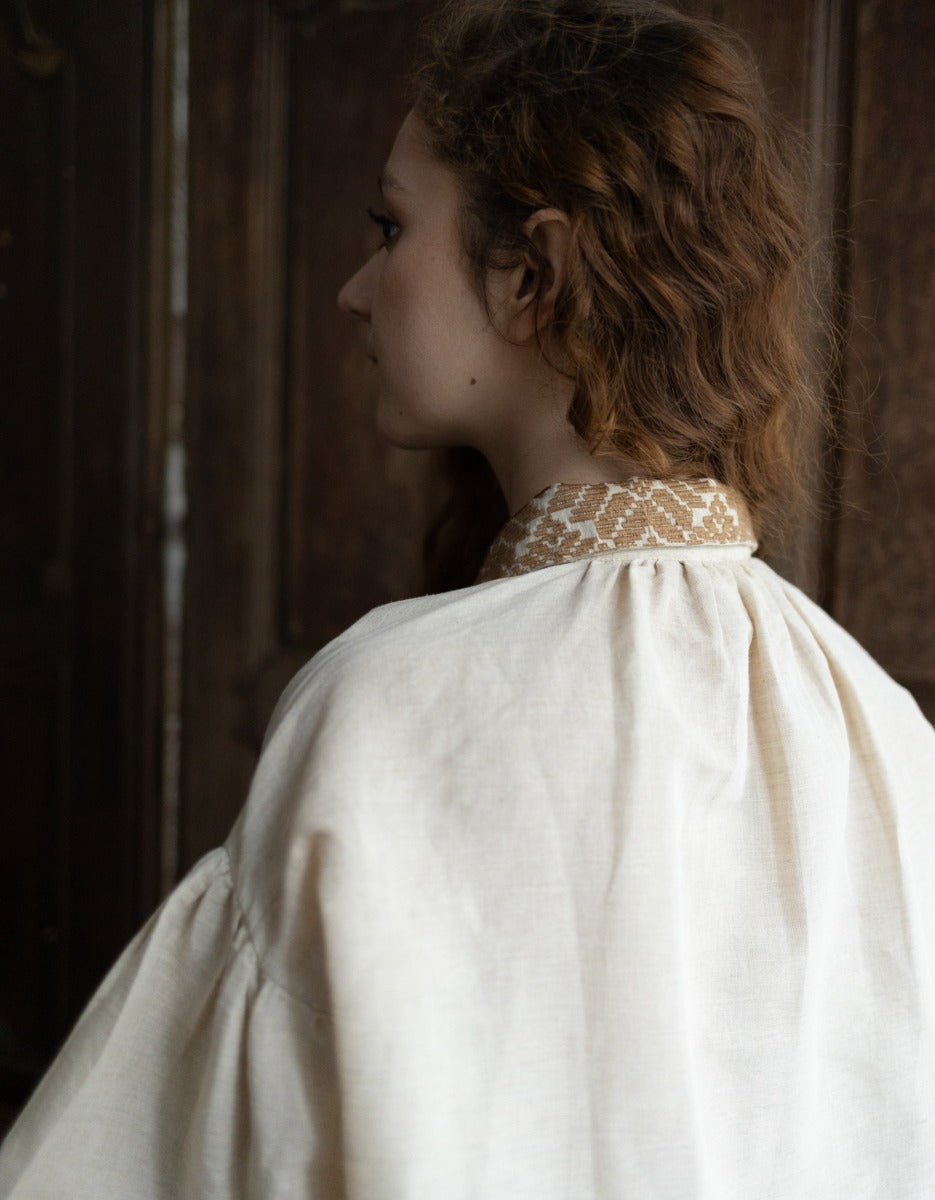 Person wearing a white dress with a high collar in a dimly lit room