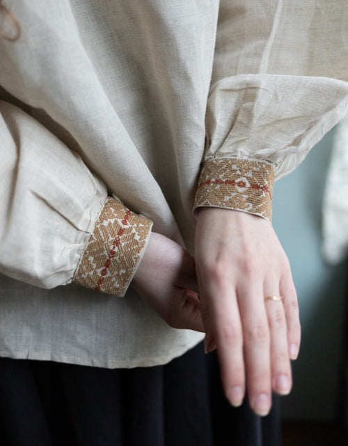 Close-up of a person wearing a beige garment with lace cuffs on the sleeves.