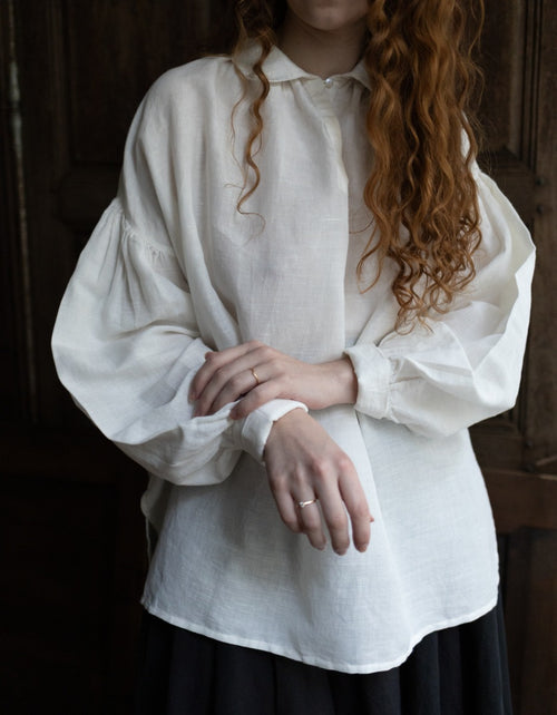 Person wearing a white blouse with long sleeves in a dimly lit setting