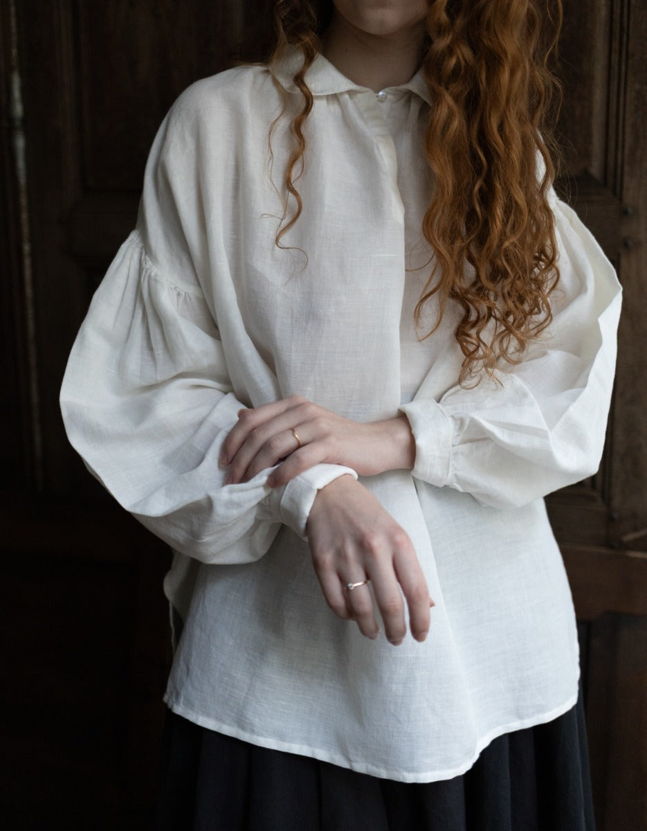 Person wearing a white blouse with long sleeves in a dimly lit setting