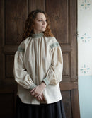 Woman wearing a historical-style blouse with intricate details in front of a wooden door.