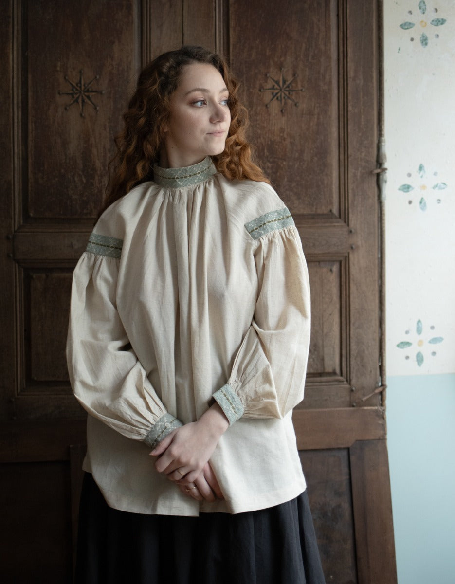Woman wearing a historical-style blouse with intricate details in front of a wooden door.