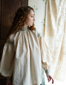 Woman wearing a historical-style dress with intricate embroidery in a softly lit room.