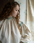 Woman wearing a beige blouse with lace details in a softly lit room.