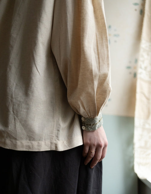 Person wearing a beige long-sleeve shirt with a blurred background