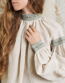 Person wearing a beige medieval-style dress with decorative cuffs and neckline.