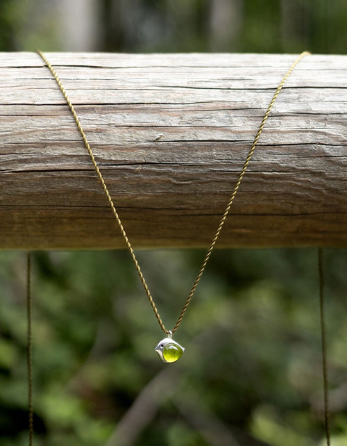 Necklace with a green pendant on a wooden log against a blurred natural background